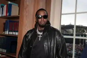 Sean Combs in Washington in 2023. He has been held in a federal detention center in Brooklyn for the past three weeks.Credit...Shareif Ziyadat/Getty Images. In this picture he is dressed in a black leather jacket and shirt. Looking around with sunglasses in a room with books in the background.