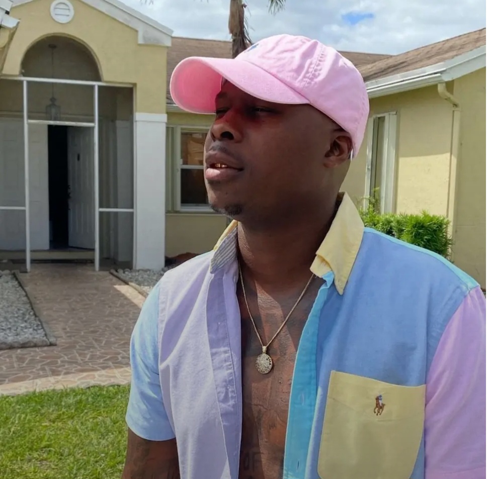 Tyrone Davis Jr. standing outside a home wearing a pink cap and a pastel button-down shirt.