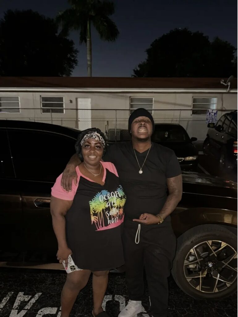 Tyrone Davis Jr stands with his mother in a parking lot at night, posing in front of a black SUV.